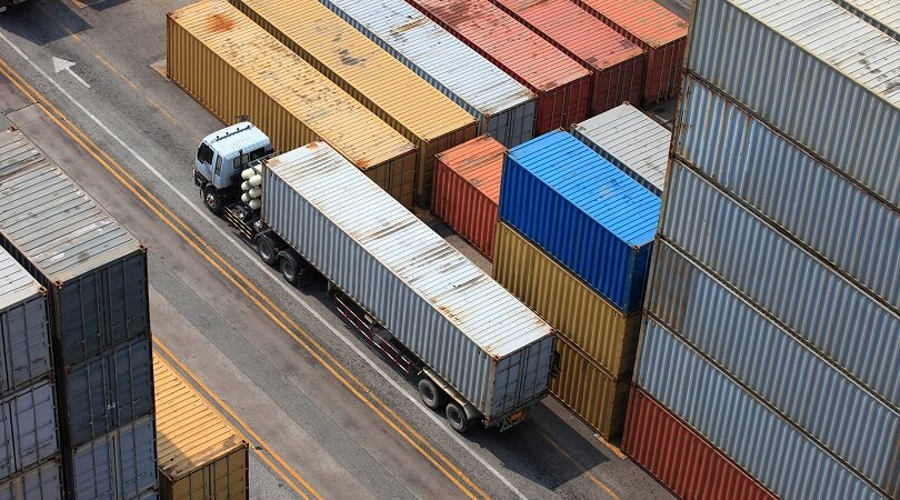 Camion transportant un conteneur entre des rangées de conteneurs empilés dans un port, illustrant les options de prix