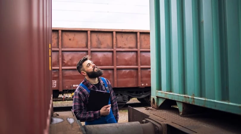Un homme avec un clipboard se tient à côté d'un train, observant attentivement les opérations ferroviaires.
